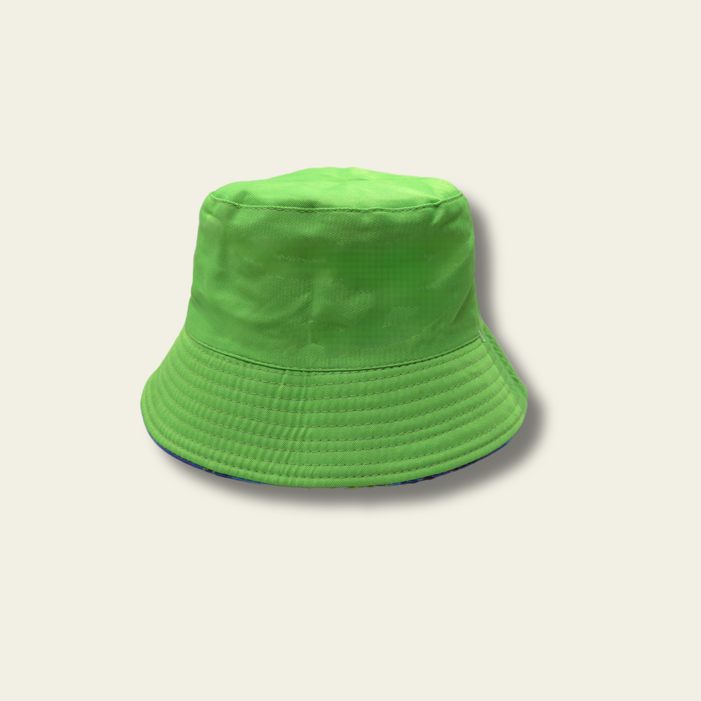 This reversible bucket hat is designed for children, offering protection from the sun with a functional and simple design. One side of the hat features a dinosaur print in shades of blue and green, while the reverse side is a solid green color. Made from lightweight fabric, the hat is breathable and provides a comfortable fit for outdoor activities.