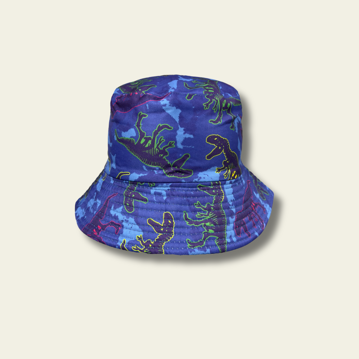 This reversible bucket hat is designed for children, offering protection from the sun with a functional and simple design. One side of the hat features a dinosaur print in shades of blue and green, while the reverse side is a solid green color. Made from lightweight fabric, the hat is breathable and provides a comfortable fit for outdoor activities.