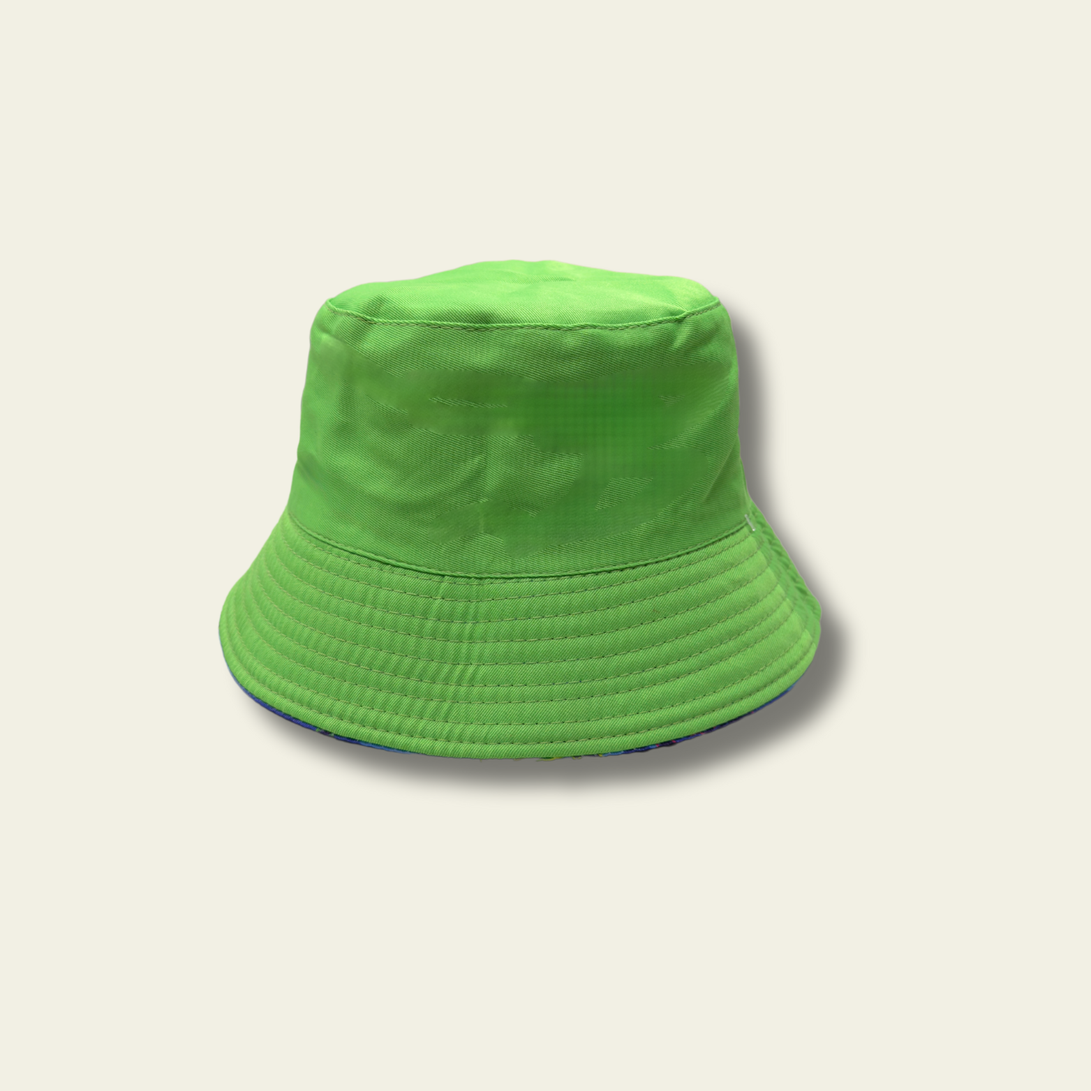 This reversible bucket hat is designed for children, offering protection from the sun with a functional and simple design. One side of the hat features a dinosaur print in shades of blue and green, while the reverse side is a solid green color. Made from lightweight fabric, the hat is breathable and provides a comfortable fit for outdoor activities.